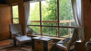 A cozy room with a large window, a wooden bench, a cushioned chair, and a small wooden chest.