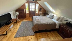 A cozy attic bedroom with a bed, a TV, a fan, and a wooden floor.