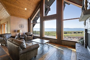Relax in a spacious living area with a high ceiling and large windows offering a panoramic view of the surrounding landscape.