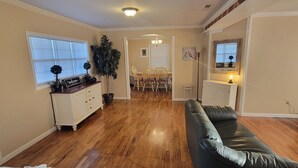 Ein Wohnzimmer mit schwarzem Ledersofa, Holzboden, einem Essbereich mit Stühlen und einer Küchenzeile mit Arbeitsplatte und Fernseher.