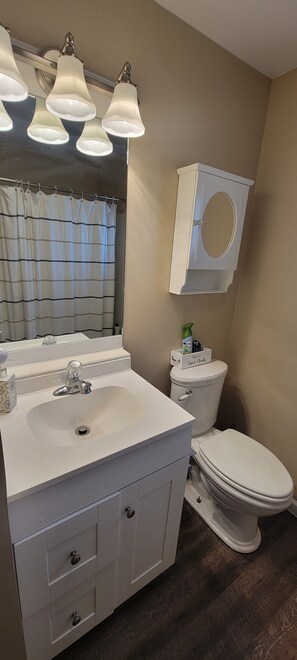 Ein Badezimmer mit weißem Waschbecken, Waschtisch und Toilette. Über dem Waschbecken sind drei Wandleuchten angebracht.