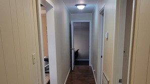 Ein Korridor mit Holzboden und weißen Wänden, der zu einem Raum mit einer Tür am Ende führt.