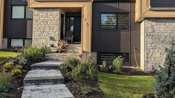 A modern multi-story house with a stone facade, a stone pathway leading to the entrance, and a well-maintained lawn.
