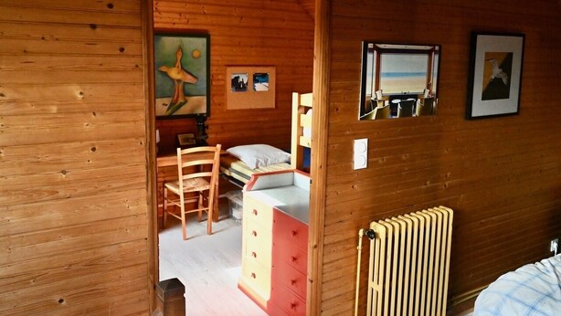 Una habitación de cabaña de madera con una cama, un tocador, una silla y una ventana con vista a la playa.