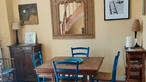 Un área de comedor con una mesa de madera y sillas azules, una alfombra, un armario y obras de arte colgadas en la pared.
