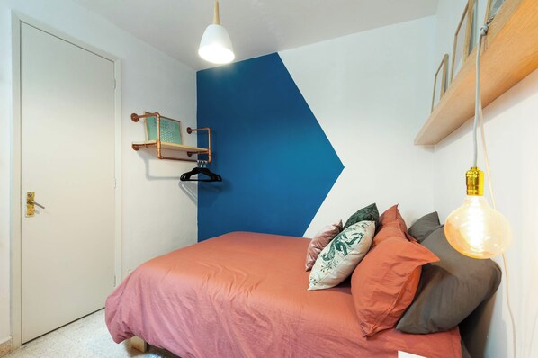 A bedroom with a bed, a hanging light, a door, and a blue wall.
