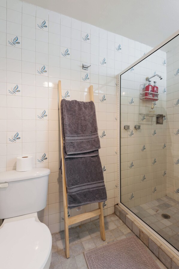A bathroom with a shower, a toilet, and a towel rack with folded towels.