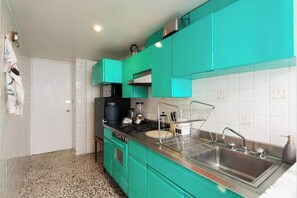 Una cocina con gabinetes verde azulado, un lavamanos de acero inoxidable y una encimera con varios electrodomésticos.
