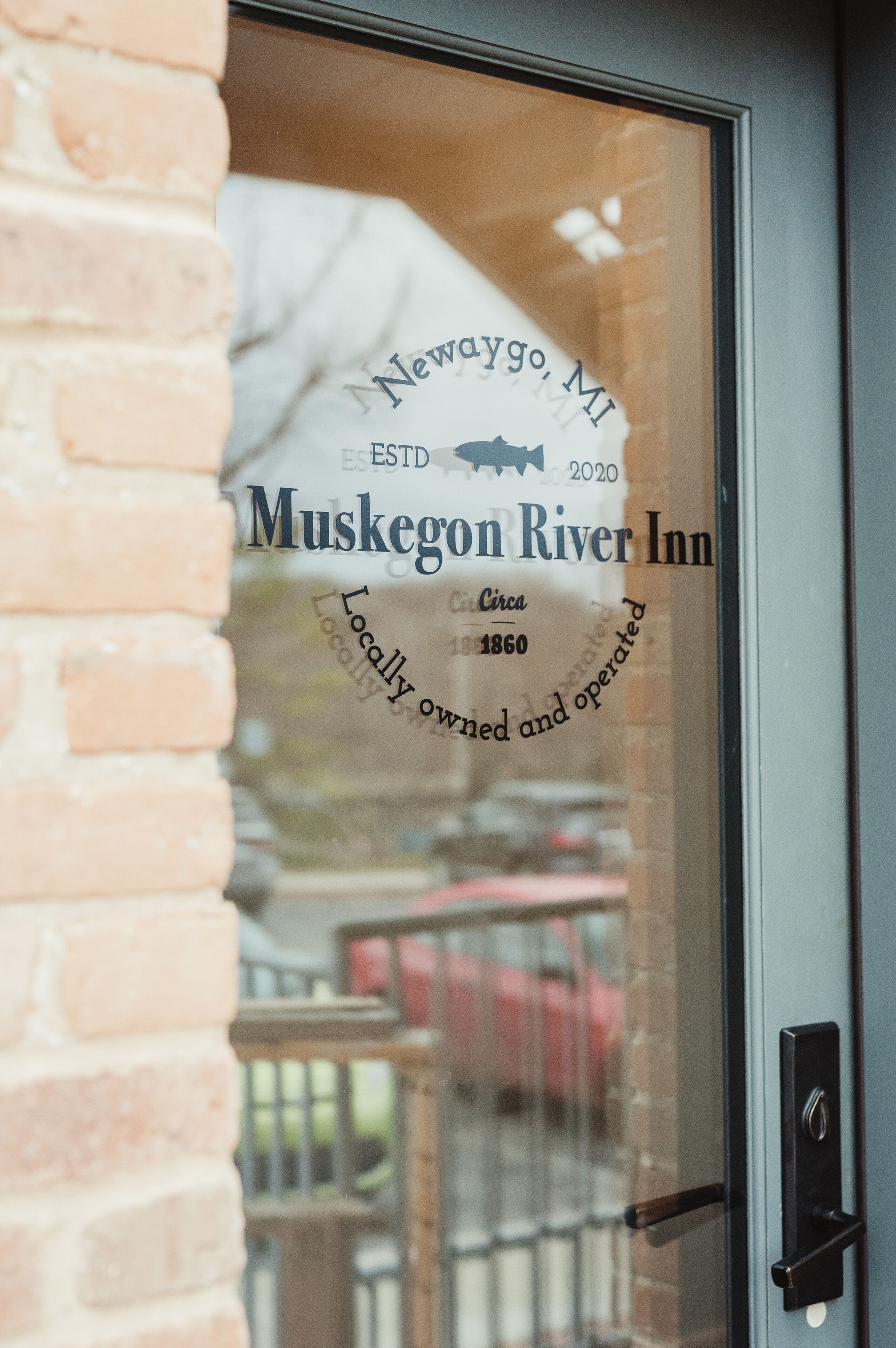 Una puerta de vidrio con el texto "Newway MI ESTD 2020 Muskgon River Inn Propiedad y operación local Desde 1860".