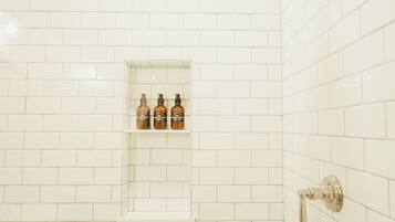 Ducha con azulejos blancos, un estante con botellas y un cabezal de ducha.