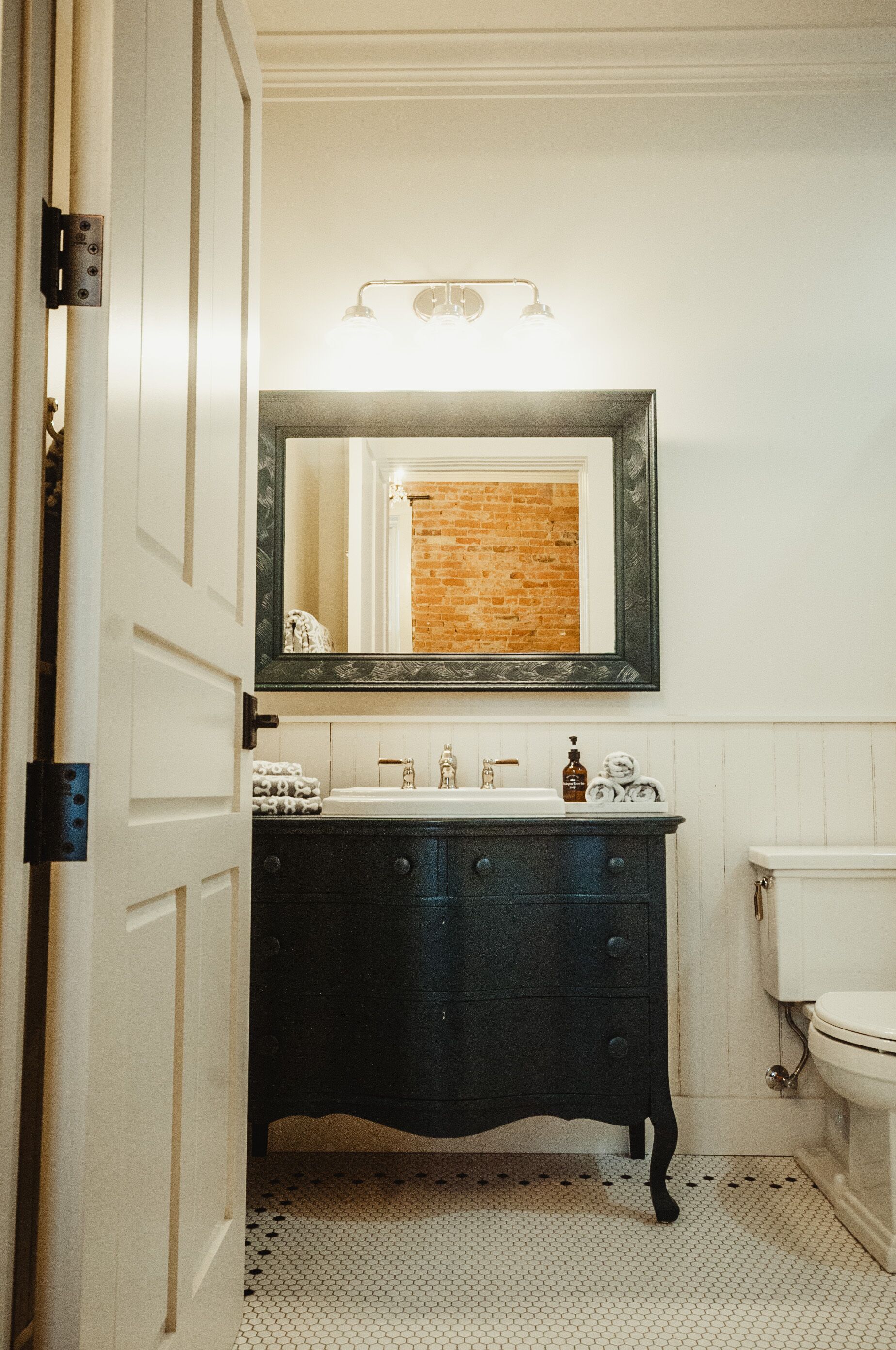 A bathroom with a white door, a black vanity with drawers, a mirror above the sink, and a white toilet.
