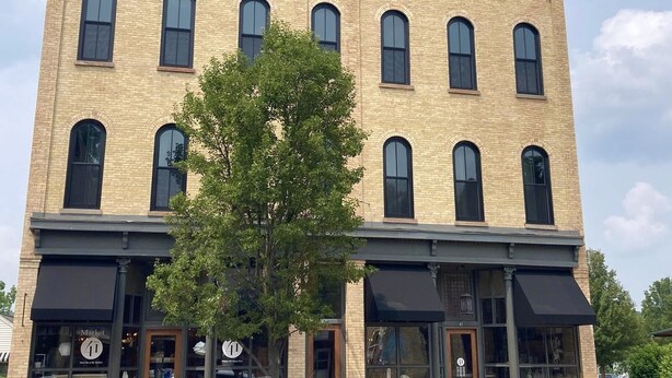 A multi-story brick building with large arched windows and awnings over the ground floor.