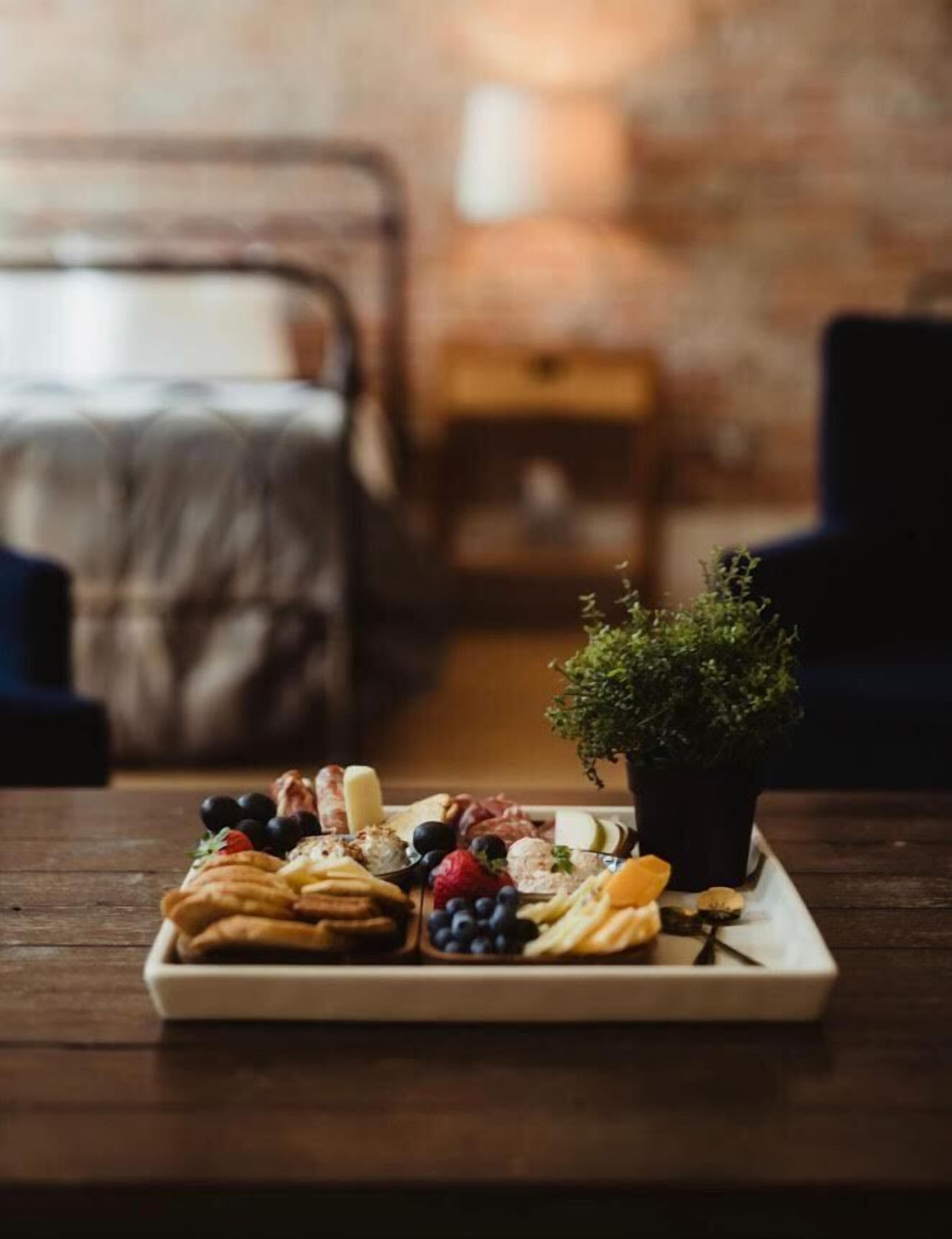 A tray of assorted snacks and fruits on a wooden table in a room with a bed and a small table in the background.