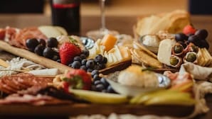 A charcuterie board with various cheeses, fruits, and meats, accompanied by a bottle of wine and a glass of red wine.