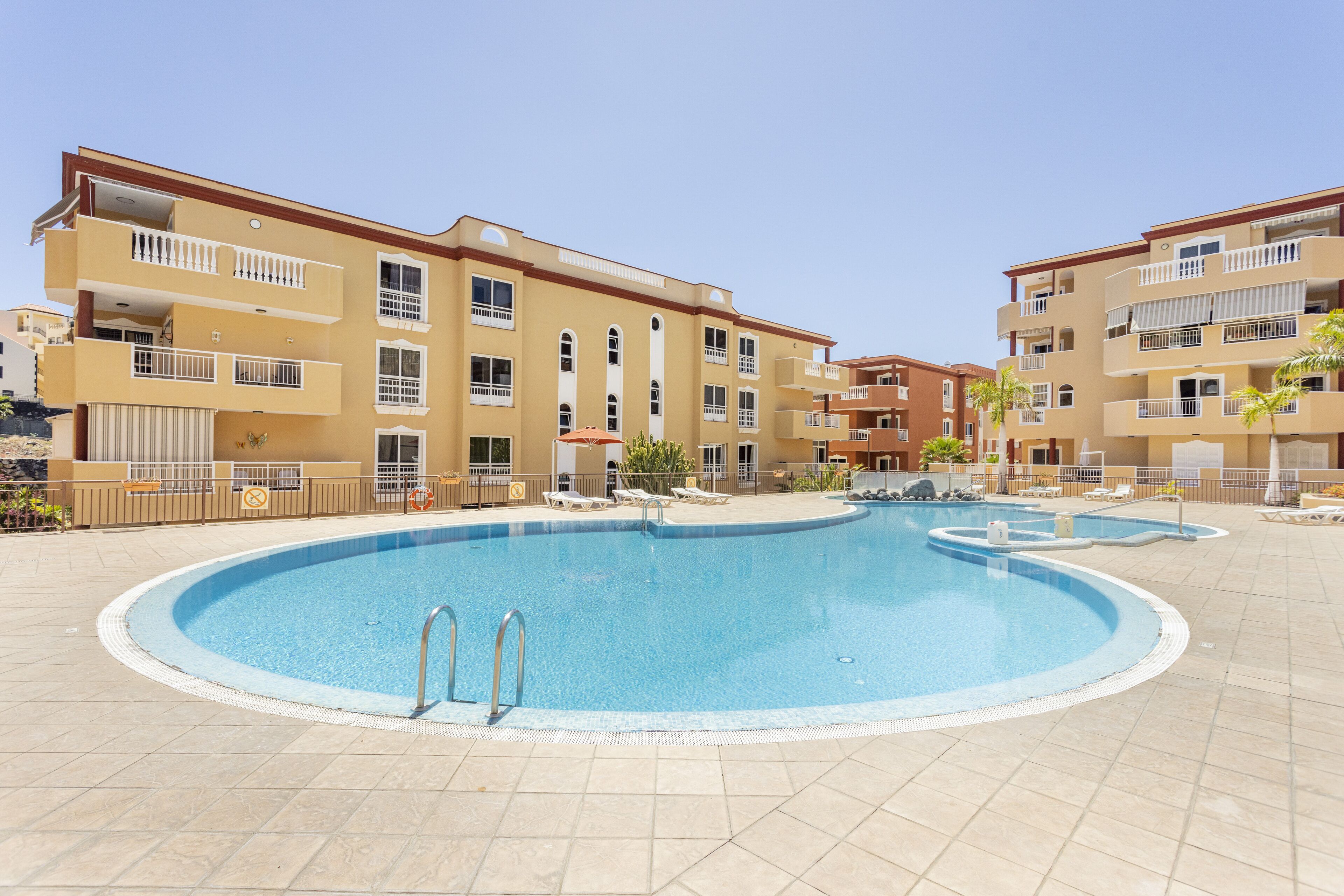 Una piscina rodeada de edificios de varios pisos con balcones y suelo de baldosas.