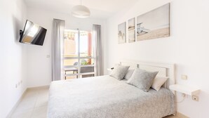 Un dormitorio con cama, televisor montado en la pared y balcón con vistas a edificios.