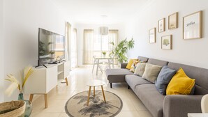 Una sala de estar moderna con un sofá, televisión y una zona de comedor con mesa y sillas.