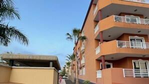 Un hotel de varios pisos con balcones, un camino empedrado y palmeras.