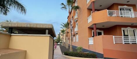 A multi-story hotel with balconies, a paved walkway, and palm trees.