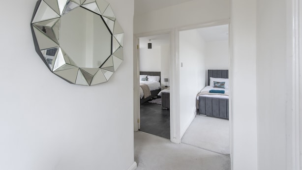 A hallway leading to a bedroom with a large mirror and a bed with a headboard. - Relax in comfort in Chingford! (Greater London)