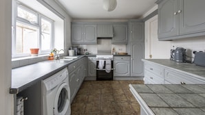 A compact kitchen with grey cabinets, a washing machine, and a window with a view. - Relax in comfort in Chingford! (Greater London)