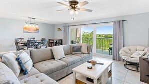 A modern living room with a sectional sofa, a dining area, and a balcony with a view. - Holiday Villas II 408 - INTERCOASTAL (Indian Shores)
