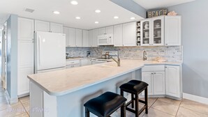 A modern kitchen with white cabinetry, a large island with bar stools, a microwave, and a sink with a faucet. - Holiday Villas II 408 - INTERCOASTAL (Indian Shores)