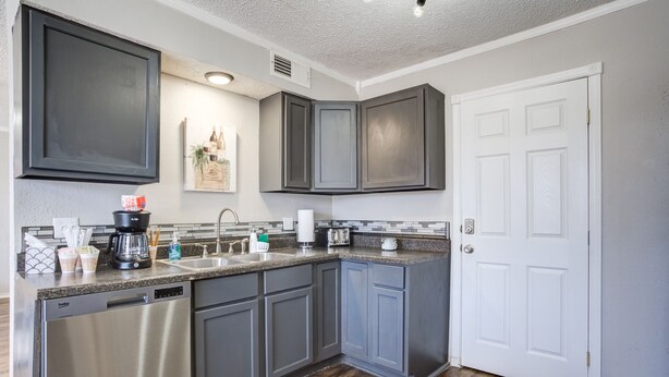 A modern kitchen with gray cabinets, stainless steel appliances, and a white door. - La Palma Guesthouse (Lubbock)