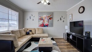 A modern living room with a sectional sofa, a flat-screen TV, a ceiling fan, and a large painting of a bull. - La Palma Guesthouse (Lubbock)