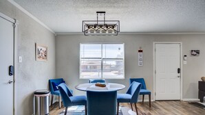 A dining area with a round table, blue chairs, a chandelier, and a window with blinds. - La Palma Guesthouse (Lubbock)