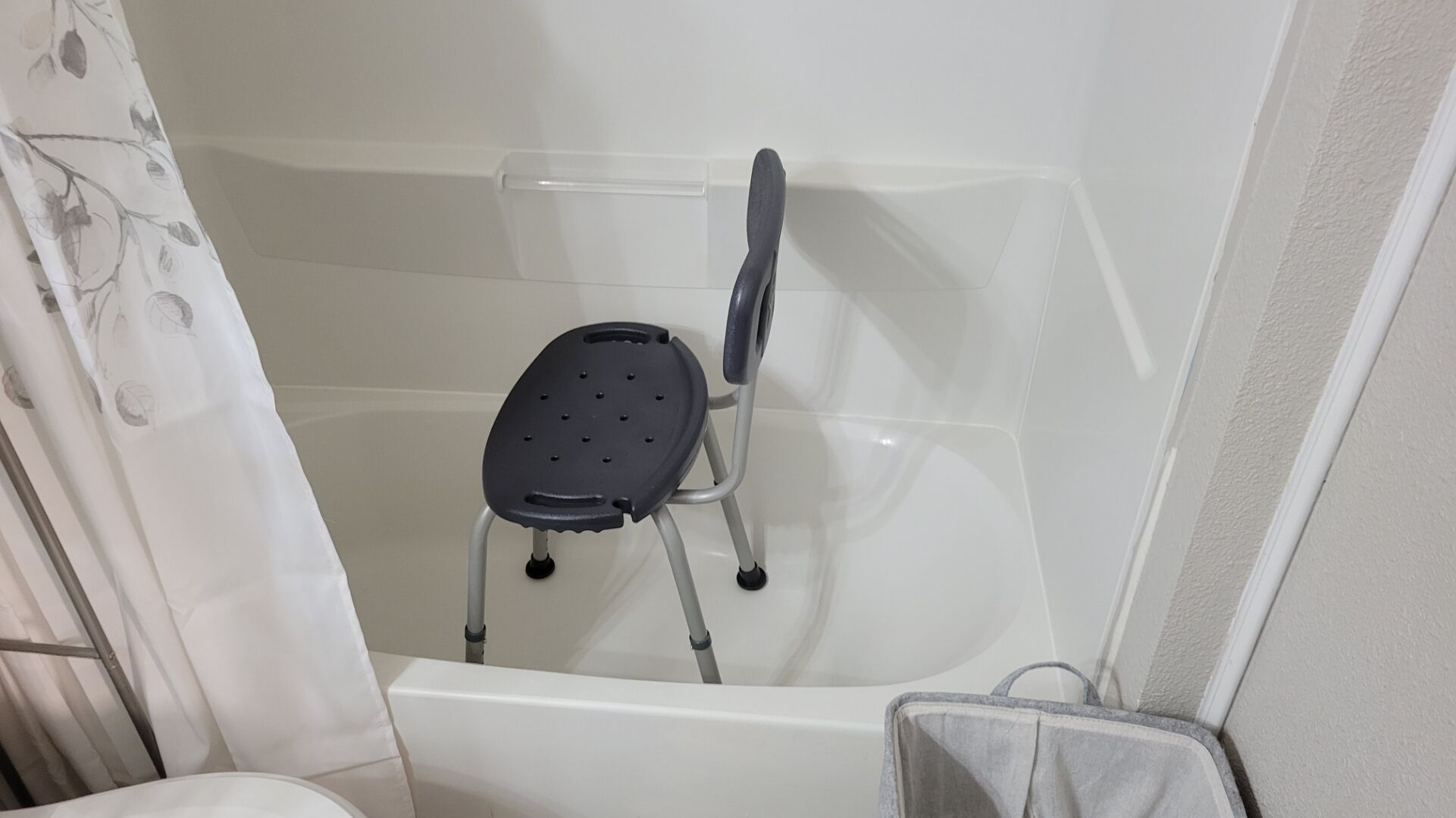 A bathroom with a shower, a white bathtub, and a black chair with wheels.
