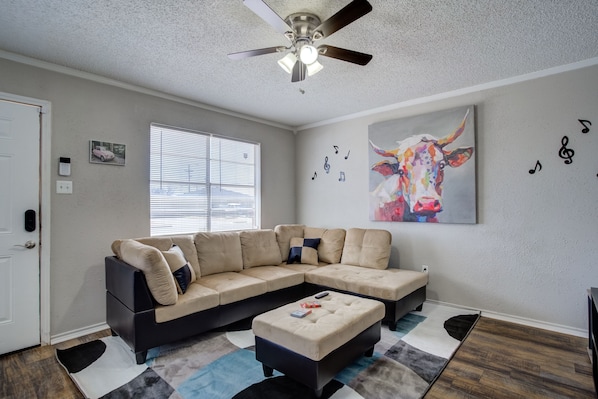 A living room with a sectional sofa, a ceiling fan, a painting, and a window with blinds.