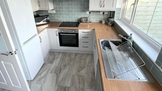 A compact kitchen with white cabinets, a built-in oven, a microwave, and a sink. - Peaceful centrally located, 2- Bedroom Bungalow. (Pengegon)