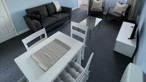 A modern living room with a sofa, two armchairs, a dining table with chairs, and a TV. - Peaceful centrally located, 2- Bedroom Bungalow. (Pengegon)