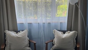 A room with two chairs, a floor lamp, and a window with sheer curtains. - Peaceful centrally located, 2- Bedroom Bungalow. (Pengegon)