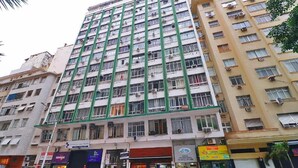 Un edificio de varios pisos con una cuadrícula de ventanas y balcones, rodeado de otros edificios y coches estacionados.