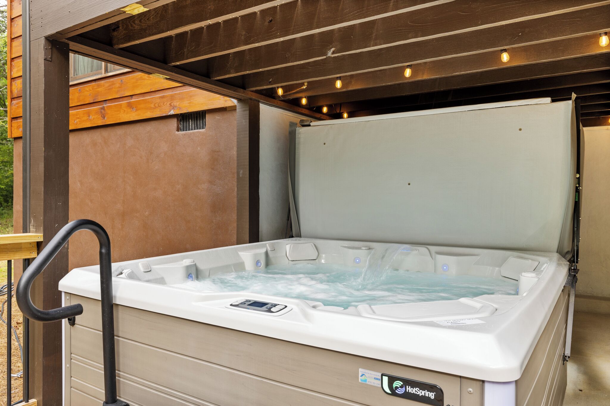 A hot tub with a control panel, a wooden deck, and a metal railing.