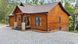 Una baita di legno con un portico in pietra, un camino e una strada di accesso sterrata.