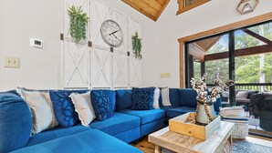 Un divano angolare blu con cuscini decorati, un tavolino in legno e un orologio a parete.