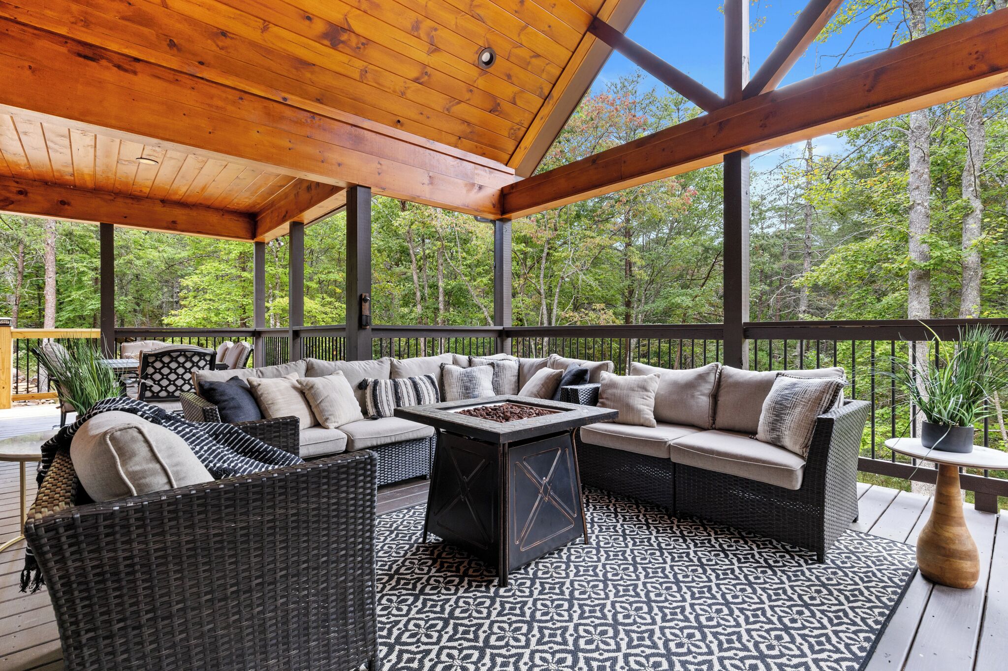 An outdoor deck with a wooden ceiling, wicker furniture, and a patterned rug.