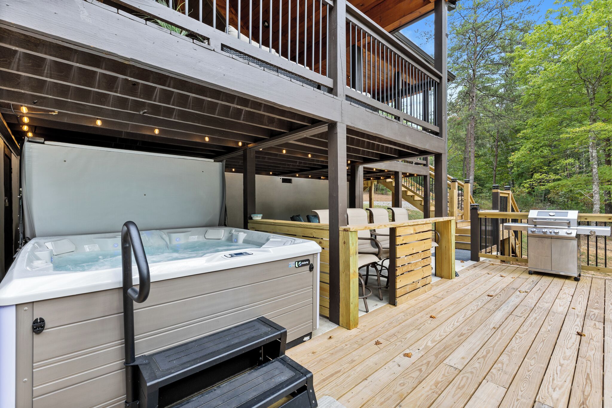 A hot tub on a wooden deck with outdoor furniture and a grill.