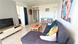 Un salon comprenant un canapé, un téléviseur et un coin repas avec des chaises et une table.