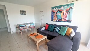 Un salon comprenant un canapé, une table basse, une table à manger avec des chaises et un tableau accroché au mur.