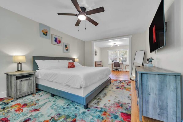 Un dormitorio con una cama, ventilador de techo, televisor y escritorio.