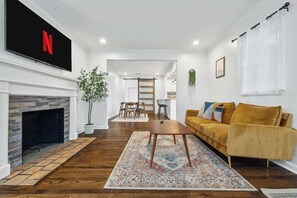 A living room with a fireplace, a sofa, a coffee table, and a TV mounted on the wall. - Modern Boho w/ 3BR/5BD Sleeps 10 (Atlanta)