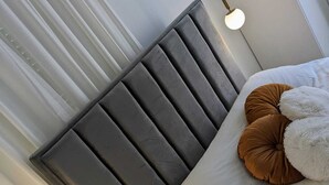 A modern bedroom with a grey upholstered headboard, white bedding, and two bedside lamps. - MORET HOUSE (Sanremo)