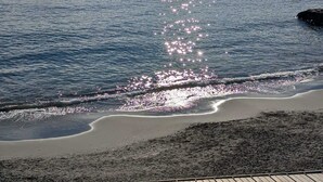 A beach with calm waters reflecting sunlight, a clear sky, and distant rocky formations. - MORET HOUSE (Sanremo)