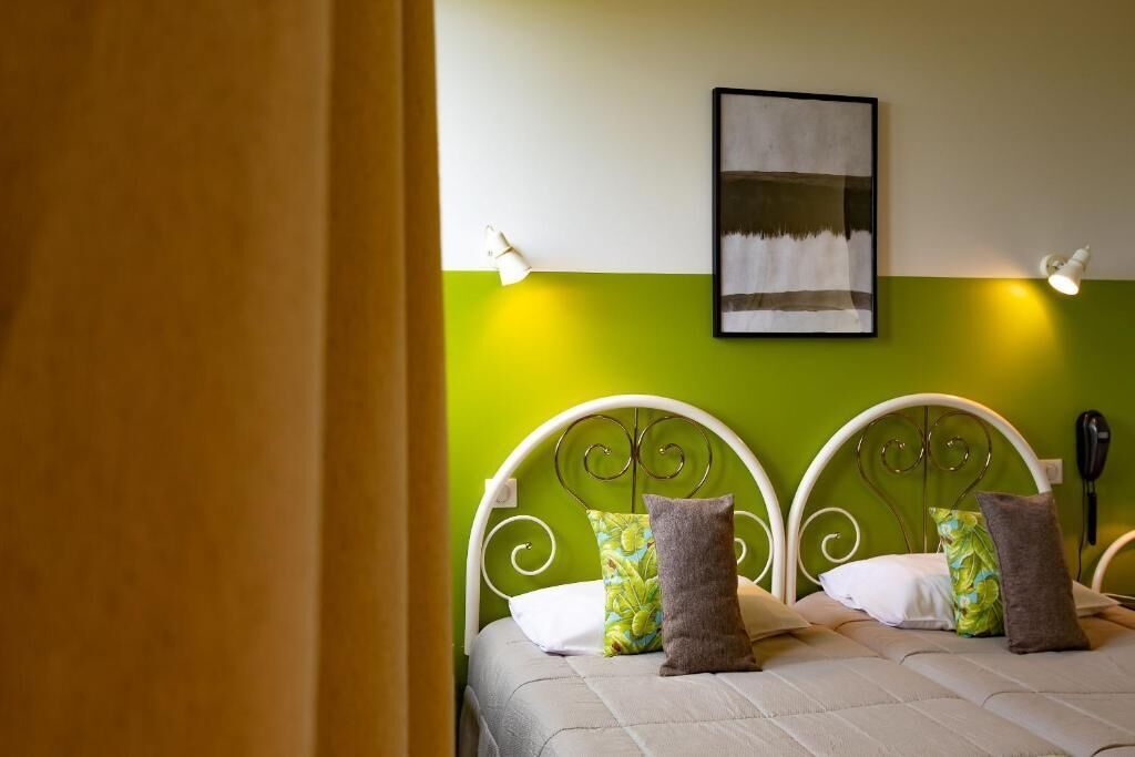 Una cama con estructura metálica blanca, paredes verdes y un cuadro enmarcado en la pared superior.