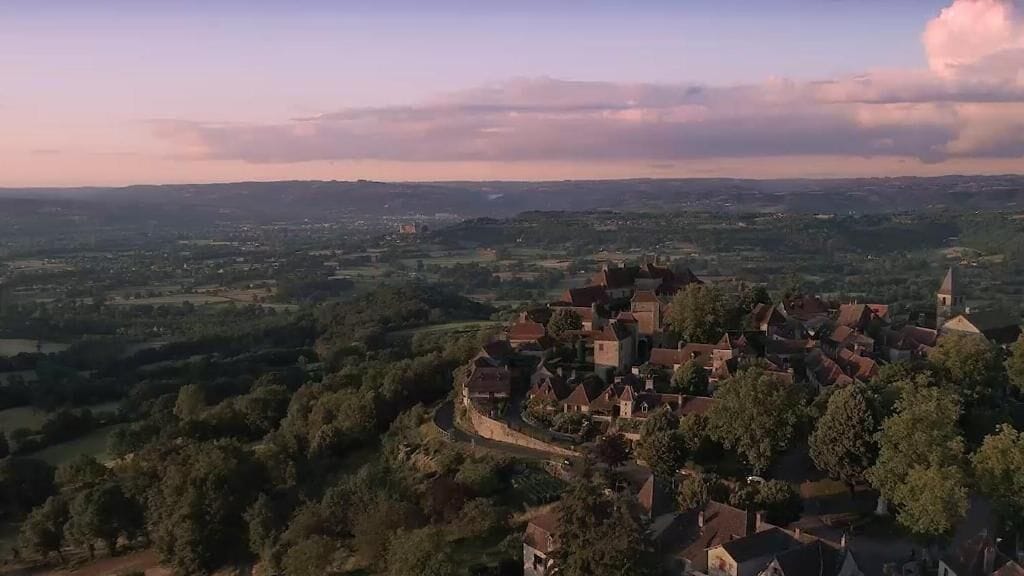 Un pueblo histórico con una iglesia central y edificios circundantes, rodeado de vegetación y colinas.