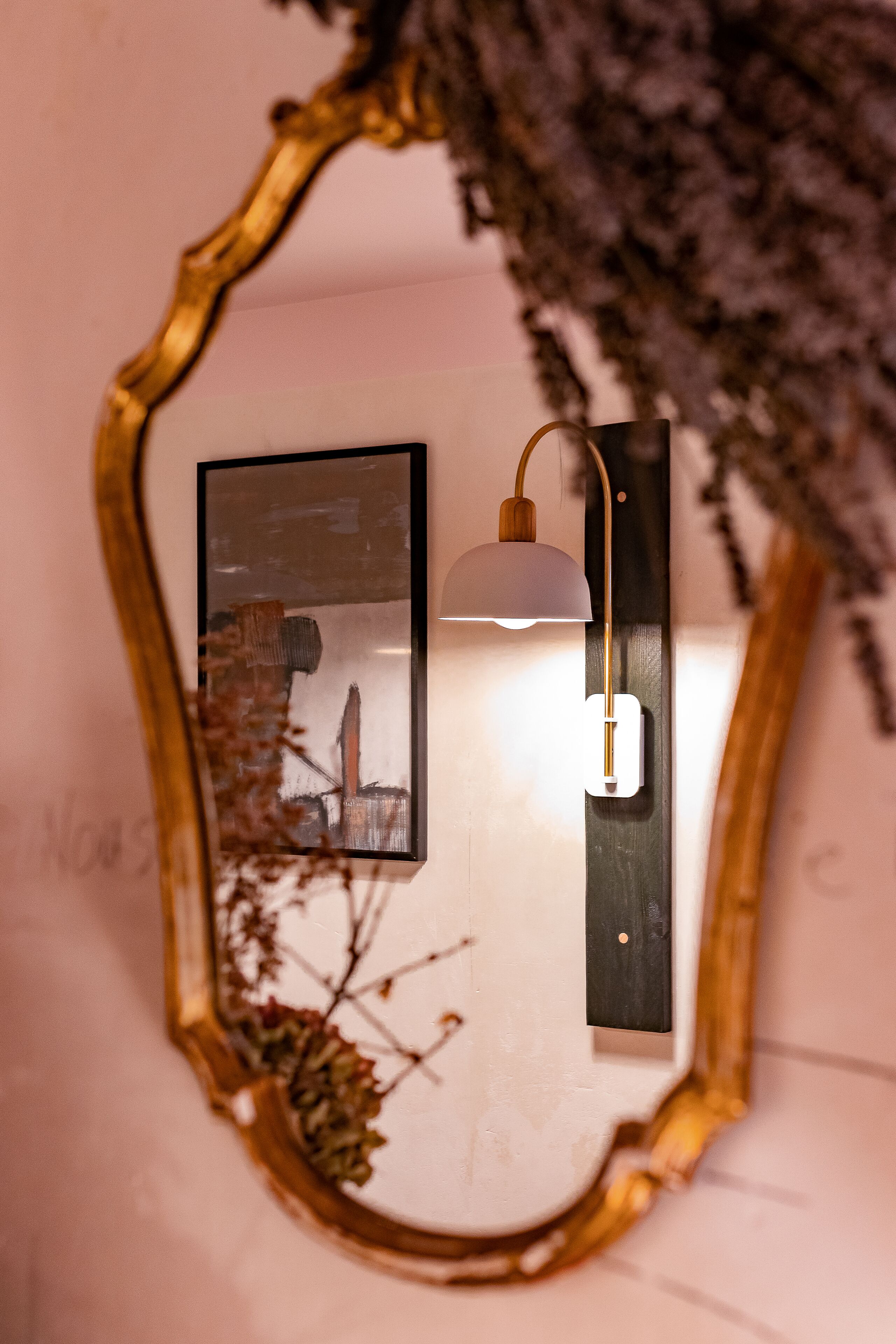 A mirror with a gold frame, a wall-mounted lamp, and a framed picture.